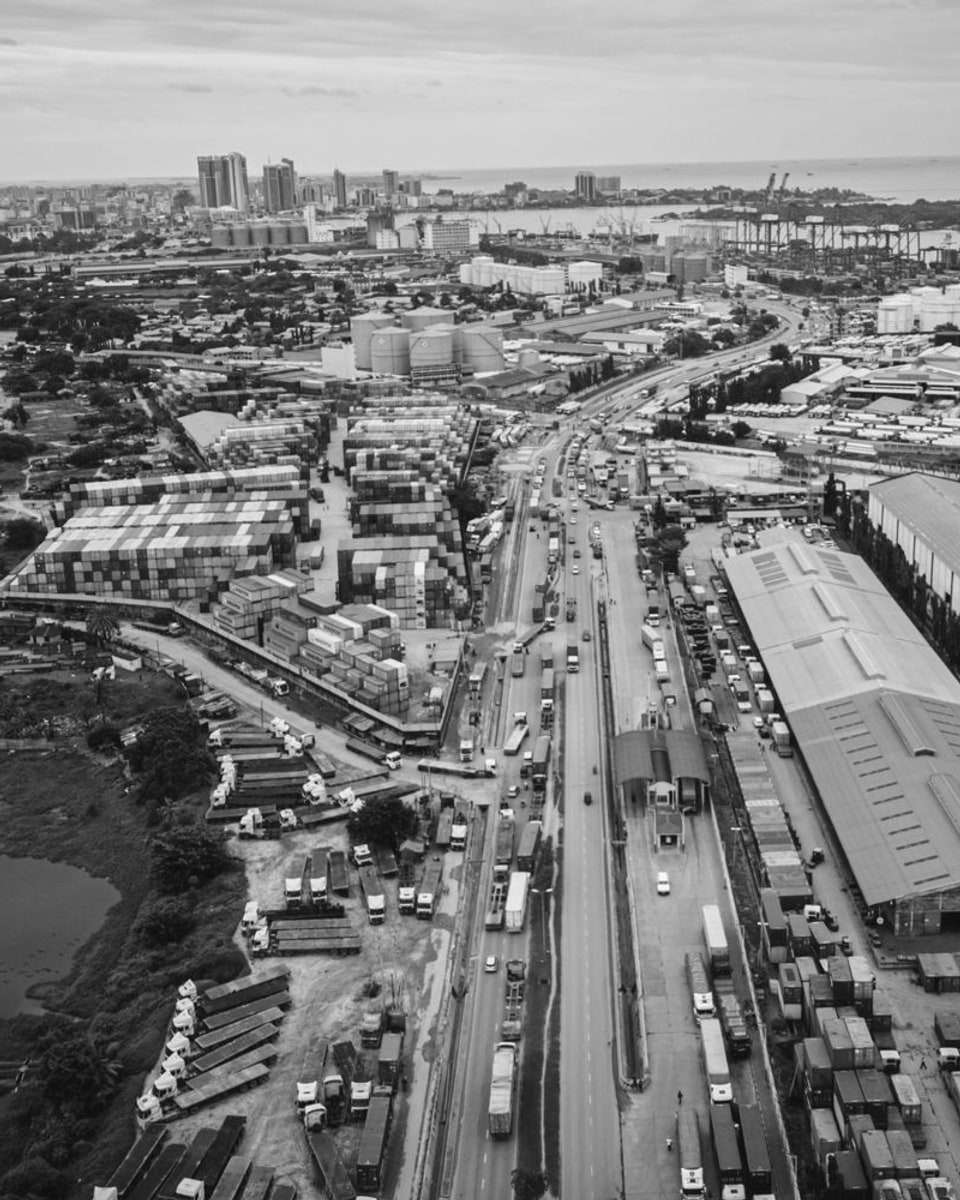 Aerial view of a port with container yards and a busy highway, and a city beyond.